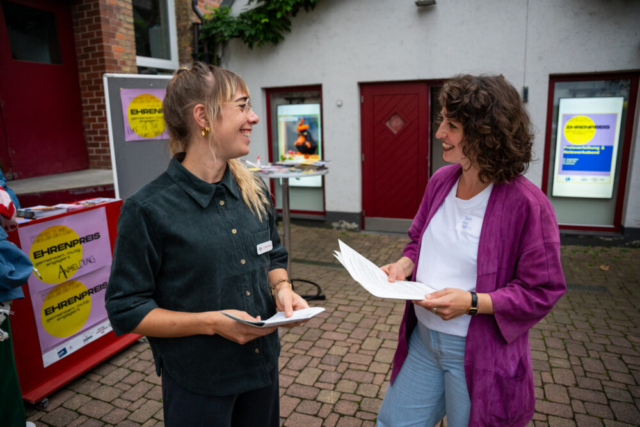 Die Moderatorinnen des Abends: Corinna Kämpfe vom Social Innovation Lab und Theresa Bath, Vorständen des Fabrik e.V.. Beide mit Zetteln in der Hand und sie sprechen miteinander